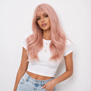 A woman modeling a long, wavy, light pink wig with straight bangs, paired with a white crop top and light blue jeans, against a plain white background.